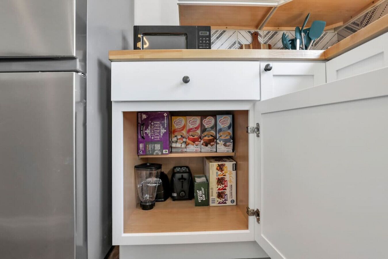 Une cuisine équipée d’une machine à café intégrée, d’un mixeur et de différents types de dosettes de café.