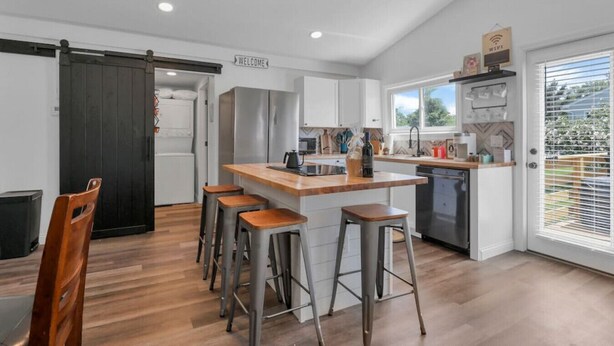 Una cocina moderna con una isla central, taburetes de bar y una entrada con puerta corredera.