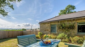 A wooden deck with a table set for breakfast, a stone building with a window, and a view of the countryside. - Shawdon Hill Cottage (Glanton, Alnwick)