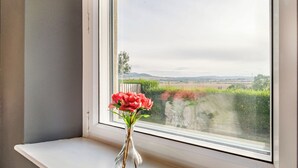 A window with a clear view of a landscape, a vase with flowers, and a white window sill. - Shawdon Hill Cottage (Glanton, Alnwick)
