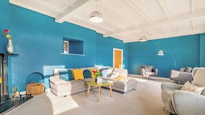 A modern living room with a blue wall, white ceiling, and a sofa with yellow cushions. - Shawdon Hill Cottage (Glanton, Alnwick)