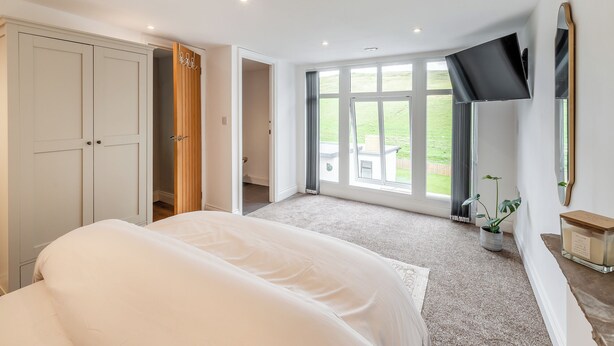 Een slaapkamer met een bed, een televisie, een groot raam en een kledingkast.