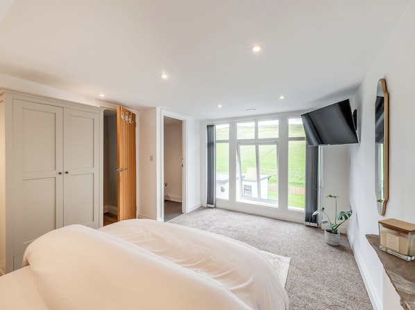 Une chambre à coucher avec un lit, une télévision, une grande fenêtre et une armoire.