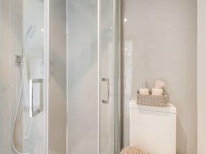A modern bathroom with a glass shower enclosure, a white toilet, and a wicker basket with toiletries.