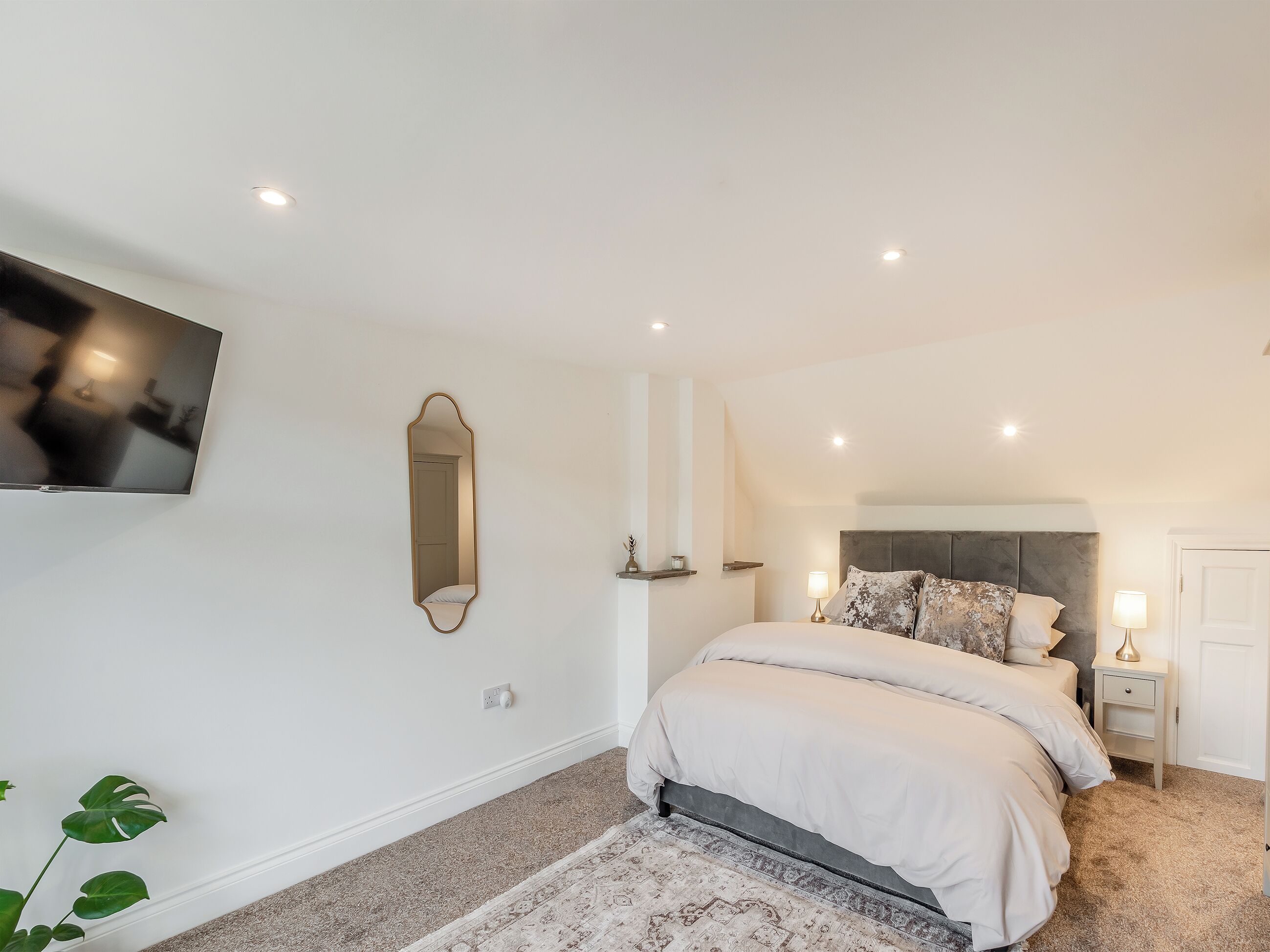 Une chambre à coucher comprenant un lit, une table de chevet, une commode, un miroir et un téléviseur fixé au mur.