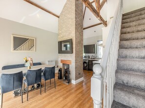 Un comedor con una mesa y sillas, una chimenea, una cocina al fondo y una escalera.