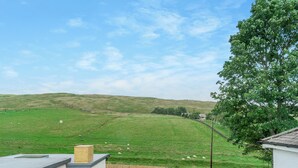 Een woonhuis met uitzicht op een groen veld en heuvels, een omheind erf en een modern gebouw met een schuin dak.