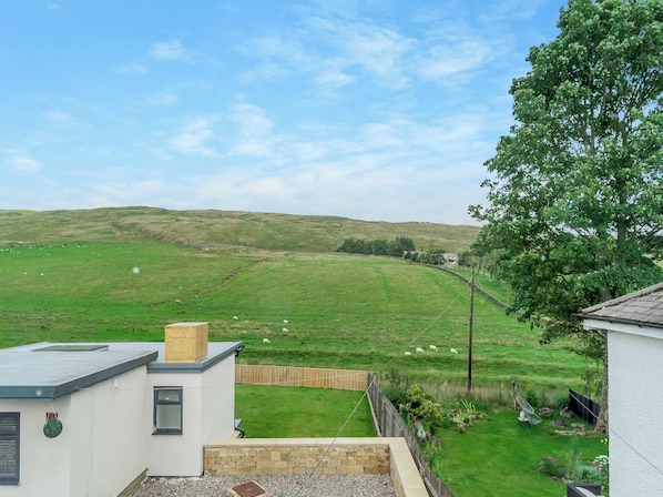 A residential property with a view of a green field and hills, a fenced yard, and a modern building with a sloped roof.