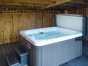 Un bain à remous dans un chalet en bois, avec un plancher et des murs en bois, et une guirlande lumineuse.