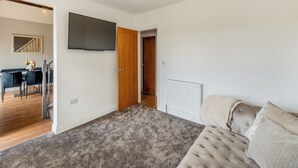 Een moderne woonkamer met een grijs tapijt, een beige bank, een flatscreen televisie en een houten deur.
