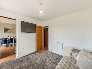 Un salon moderne avec un tapis gris, un canapé beige, un téléviseur à écran plat et une porte en bois.