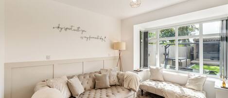 Une pièce confortable avec une grande fenêtre, un canapé, un fauteuil de lecture et un élément décoratif mural.