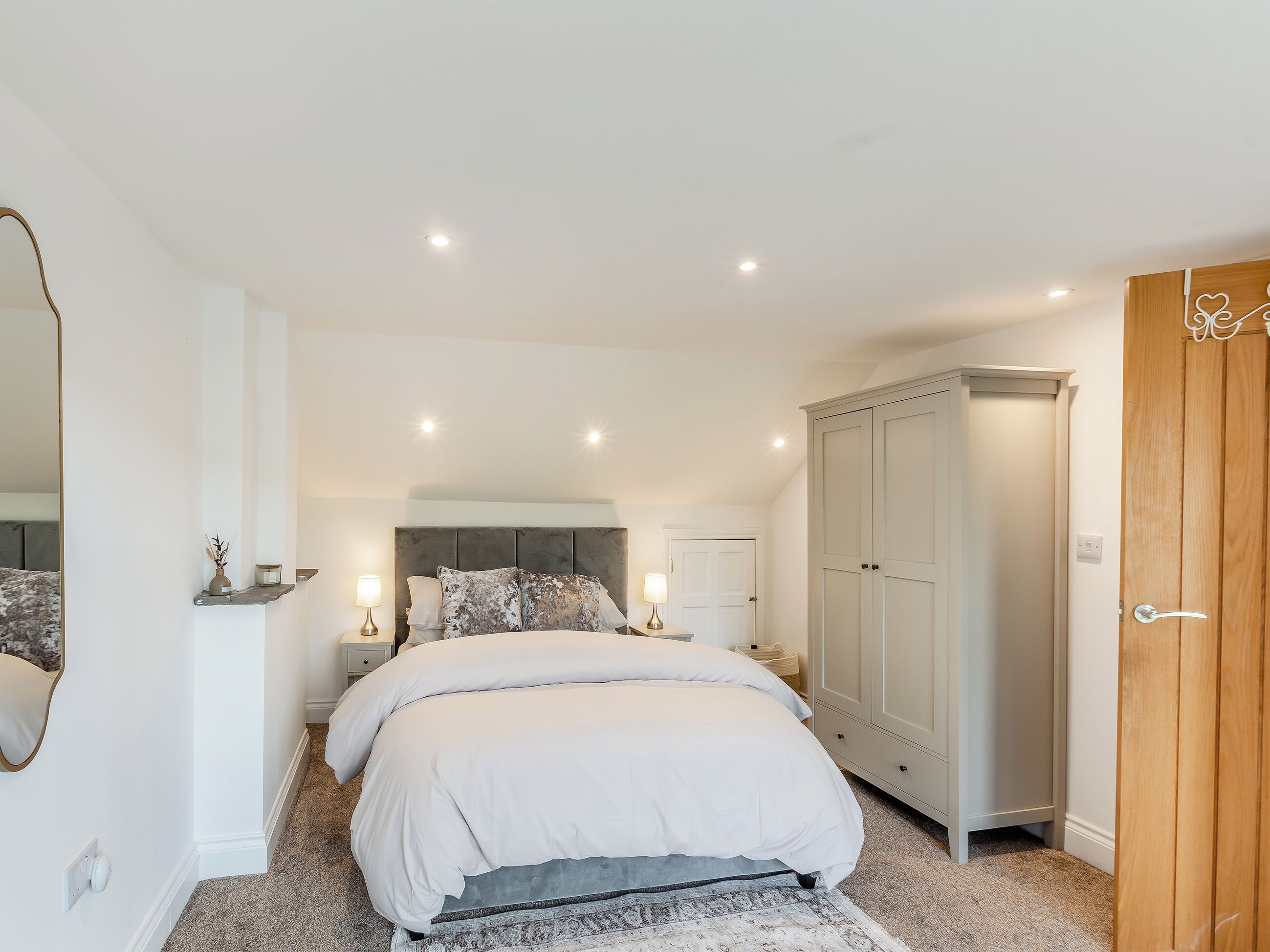 Een slaapkamer met een bed, nachtkastjes, een kledingkast en een spiegel.