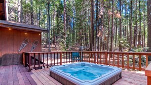 Un bain à remous sur une terrasse en bois, entouré d’une forêt.