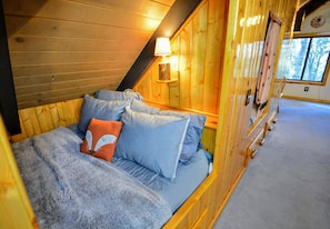 Quarto de cabana de madeira acolhedor, com cama, almofadas, abajur e janela.