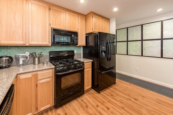 A modern kitchen with wooden cabinets, a stainless steel refrigerator, a microwave, a stove, and a coffee maker.