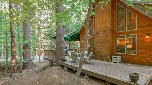 Una cabaña de madera con terraza, mobiliario exterior y vistas al bosque circundante.