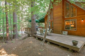 A wooden cabin with a deck, outdoor seating, and a view of the surrounding forest.