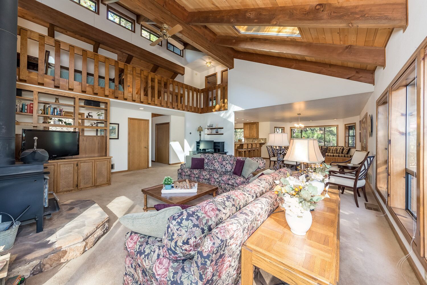 A spacious living area with a high ceiling, wooden beams, a fireplace, a television, and a cozy seating arrangement.
