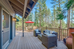 A wooden deck with outdoor furniture, a red umbrella, and a view of tall pine trees.