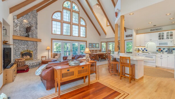 A spacious living area with a fireplace, large windows, and a kitchen with white cabinets. - Bear House - Walking Distance to Snowflake Lodge, Pool,Lake and Recreation! (Arnold)