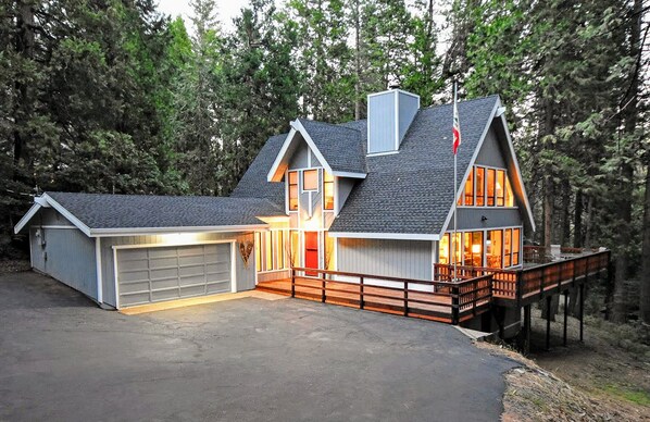 A two-story house with a garage, a covered porch, and a deck extending over a forested area. - Dancing with Trees - Large 4 bedroom 3 Bath home in Blue Lake Springs! (Arnold)
