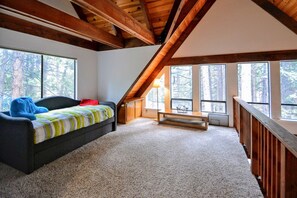 A bedroom with a sloped ceiling, large windows, a bed, a bench, and a view of the forest. - Dancing with Trees - Large 4 bedroom 3 Bath home in Blue Lake Springs! (Arnold)
