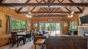A cozy cabin interior with a wooden ceiling, a sofa, a dining table, and a fireplace. - Cabin in Blue Lake Springs & Steps Away From Fly-In Lake (Arnold)