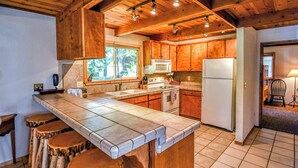 A kitchen with wooden cabinets, a large island with stools, a microwave, and a refrigerator. - HUGGING TREES - 4 BEDROOM 2 full, 2 half  BATH WITH GAME ROOM, SLEEPS 12 (Arnold)