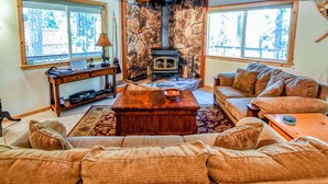 A cozy living room with a stone fireplace, comfortable seating, and large windows. - HUGGING TREES - 4 BEDROOM 2 full, 2 half  BATH WITH GAME ROOM, SLEEPS 12 (Arnold)