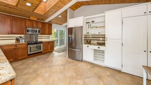 Een moderne keuken met houten kastjes, roestvrijstalen apparatuur en een groot raam.