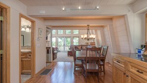 A spacious kitchen with wooden cabinets, a dining area with a table and chairs, and a view of the outdoors through large windows. - Lazy Bear Lair - Prime Location in Blue Lake Springs with Air Conditioning! (Arnold)