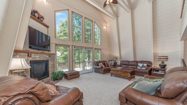 A spacious living room with high ceilings, large windows, a fireplace, leather sofas, and a flat-screen TV. - Lazy Bear Lair - Prime Location in Blue Lake Springs with Air Conditioning! (Arnold)
