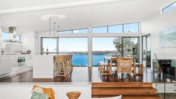 A modern kitchen with a large island, wooden dining table, and chairs, overlooking a scenic view.