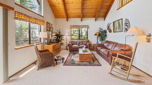 Un salon spacieux avec un haut plafond en bois, de grandes fenêtres, un canapé en cuir marron, un fauteuil à bascule en bois et une petite table basse.