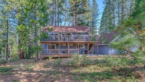 A two-story cabin with a deck, surrounded by tall pine trees.