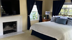 A bedroom with a fireplace, a bed with patterned pillows, and a large window with curtains. - Beach, bay, town, walking distance.  Large private fenced in home (Coronado)