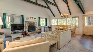 Un salón amplio con chimenea, asientos cómodos, televisor y ventanas grandes.