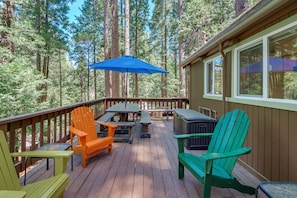 A wooden deck with outdoor furniture, including chairs and a table, surrounded by tall trees.