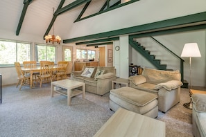 A spacious living room with a high ceiling, a dining area with wooden chairs, a sofa set, and a staircase leading to another level.