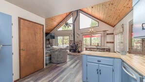 Un'ampia cucina con soffitto in legno, una zona pranzo con tavolo e sedie, e un angolo salotto accogliente con camino.