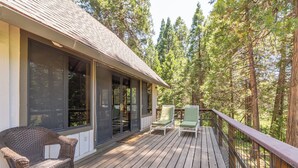 A wooden deck with two green cushioned chairs and a wicker chair, overlooking a forested area. - Coyote Den - Pet Friendly Home w/ Game Room and Fenced Backyard and Game Room! (Arnold)