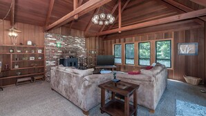 A rustic living room with a stone wall, wooden beams, a large sofa, a television, and a fireplace. - Coyote Den - Pet Friendly Home w/ Game Room and Fenced Backyard and Game Room! (Arnold)