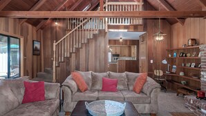 A spacious living room with a high ceiling, wooden beams, a staircase, and a kitchen in the background. - Coyote Den - Pet Friendly Home w/ Game Room and Fenced Backyard and Game Room! (Arnold)