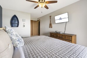 A bedroom with a bed, a ceiling fan, a dresser, and a TV mounted on the wall.