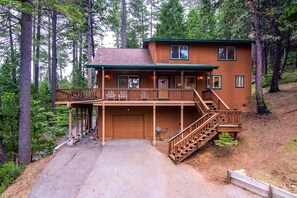 A two-story log cabin with a front porch, a covered deck, and a staircase leading to the upper level.