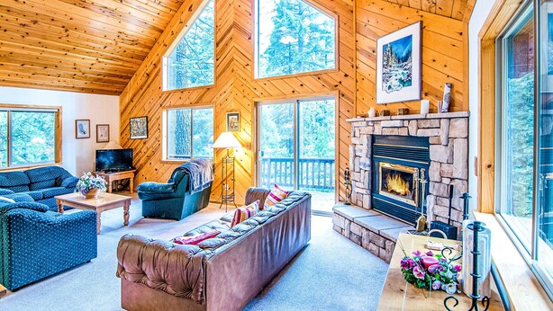Un intérieur de chalet chaleureux avec une cheminée, de grandes fenêtres et un coin salon confortable.
