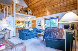 A spacious living room with a high ceiling, a staircase, and a dining area.
