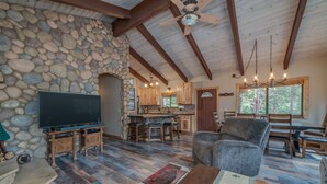 Ein rustikales Interieur mit einer Steinwand, Holzbalkendecke, einem Flachbildfernseher, einem Steinkamin und einer Essecke mit Holzmöbeln.