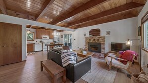 Un ampio soggiorno con camino, travi in legno a soffitto, un divano e una zona pranzo con cucina sullo sfondo.